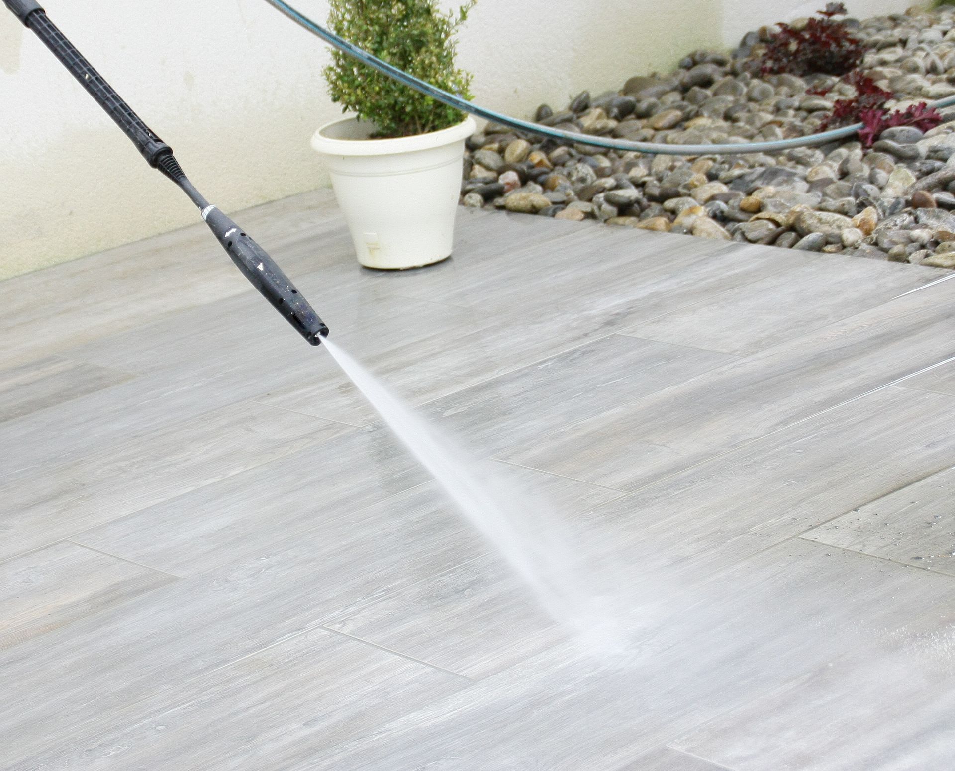 Nettoyage à haute pression d'une terrasse gris clair jouxtant une jardinière blanche et un jardin de rocaille.