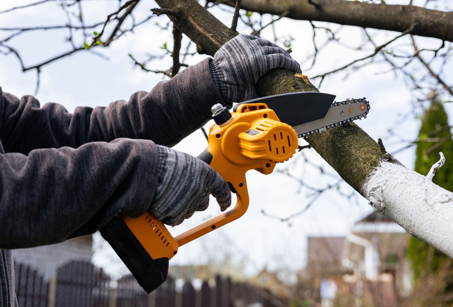 Des mains gantées utilisent une tronçonneuse sans fil jaune pour couper une branche d'arbre.