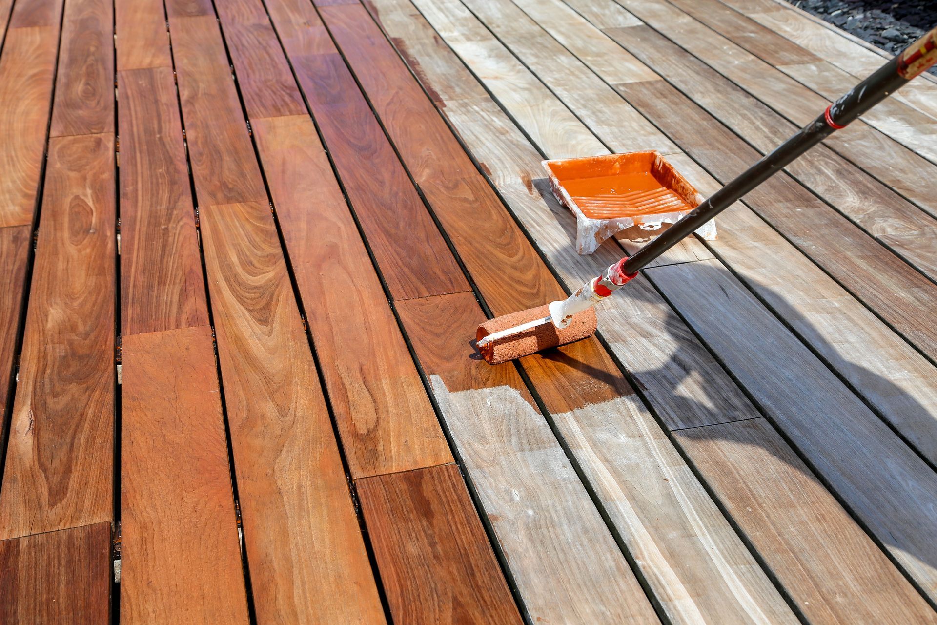 Une personne applique une lasure sur une terrasse en bois à l'aide d'un rouleau.