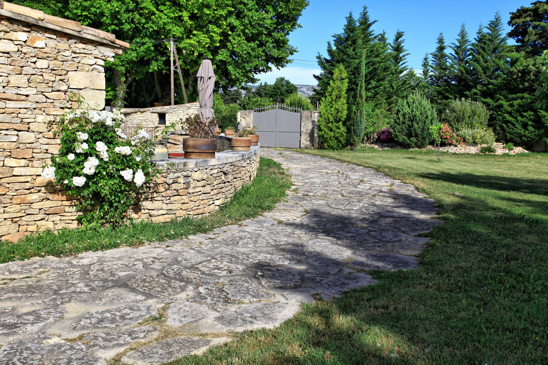 Une allée en pierre serpente à travers un jardin paysager et longe un mur de pierre.