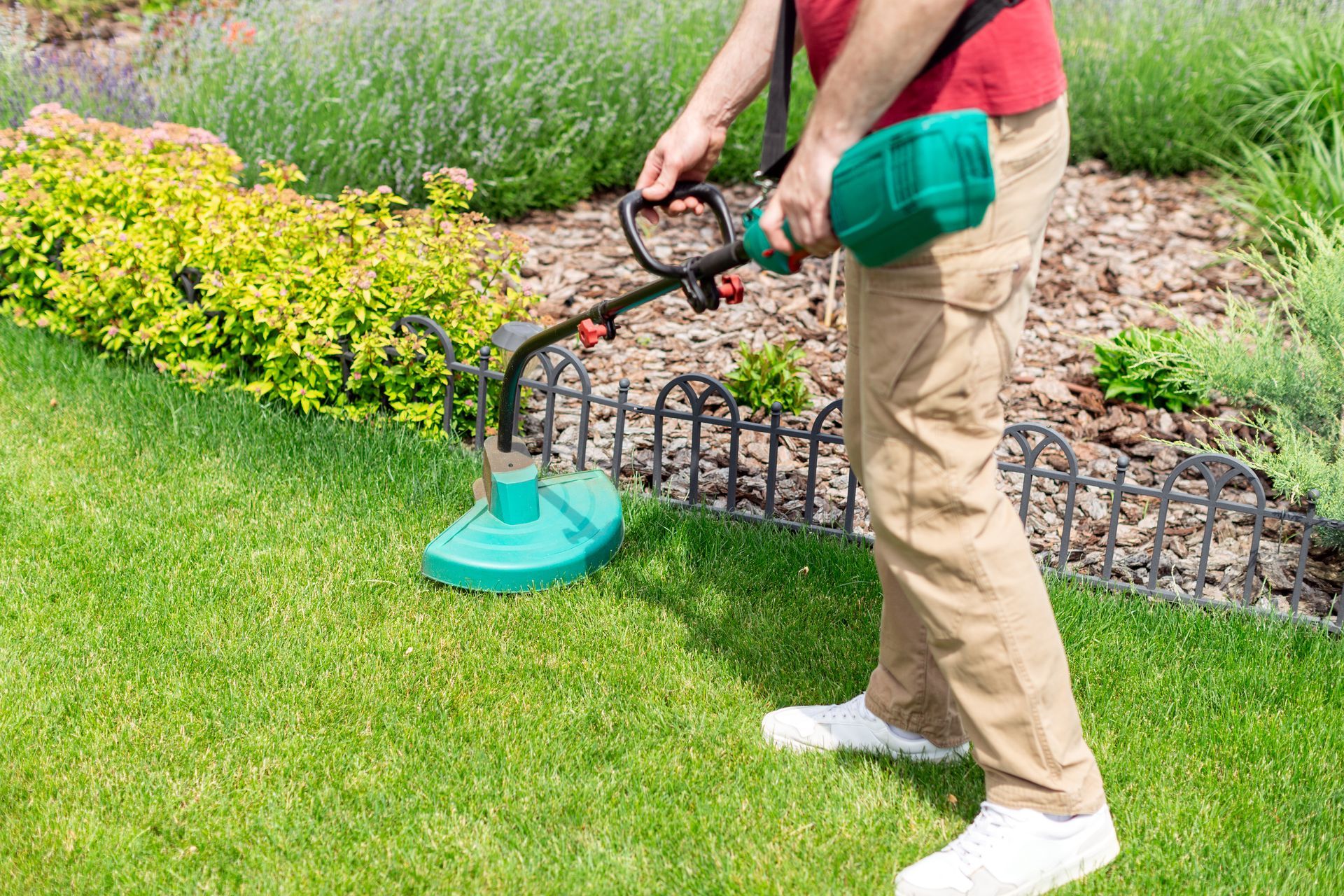 Une personne utilise un coupe-bordures à fil vert le long d'une bordure de pelouse dans un jardin.