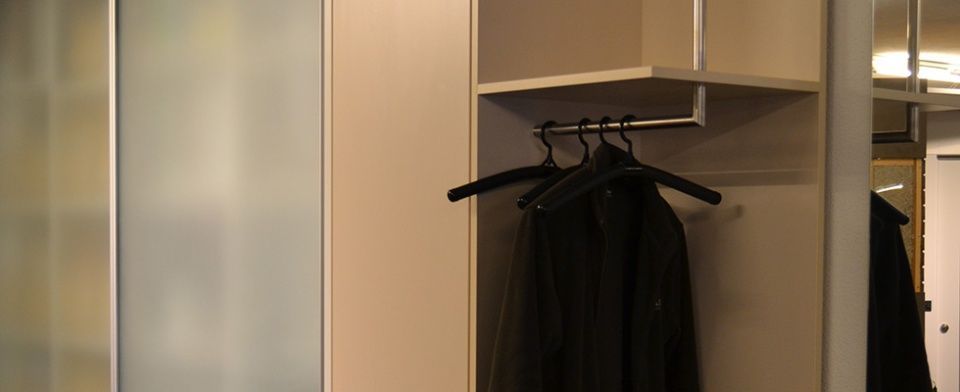 Ein Schrank mit an einer Stange hängender Kleidung und einem Spiegel.