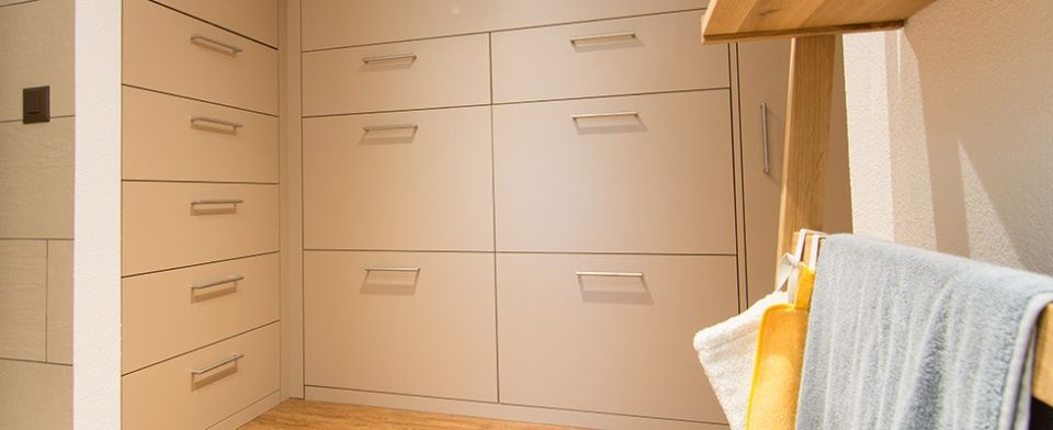 Ein begehbarer Kleiderschrank mit vielen Schubladen und einem Holzregal.