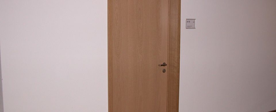 In einem Raum steht eine Holztür zu einer weissen Wand offen.