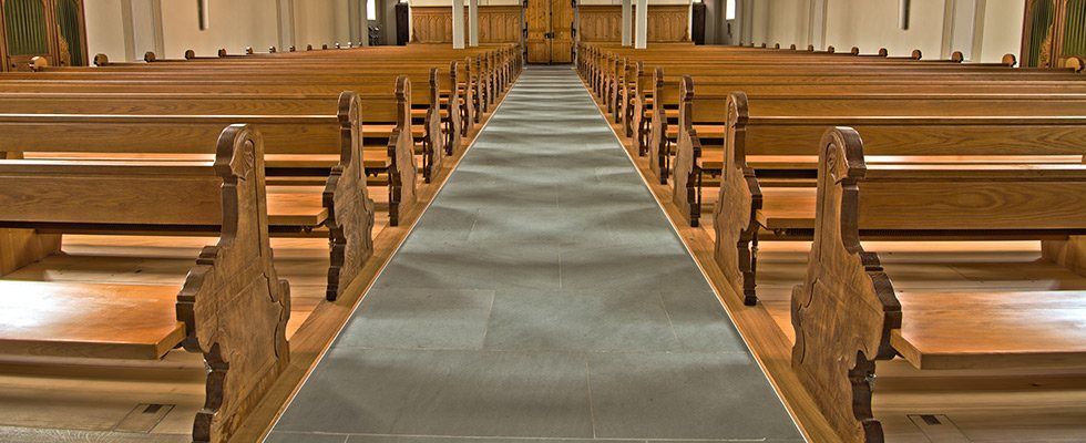 Eine Kirche mit Reihen von Holzbänken und einem grauen Teppich.