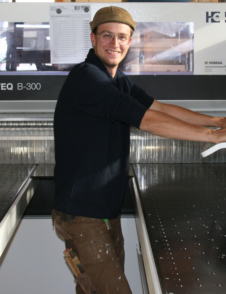 Ein Mann mit Hut und Brille lehnt an einem Tisch