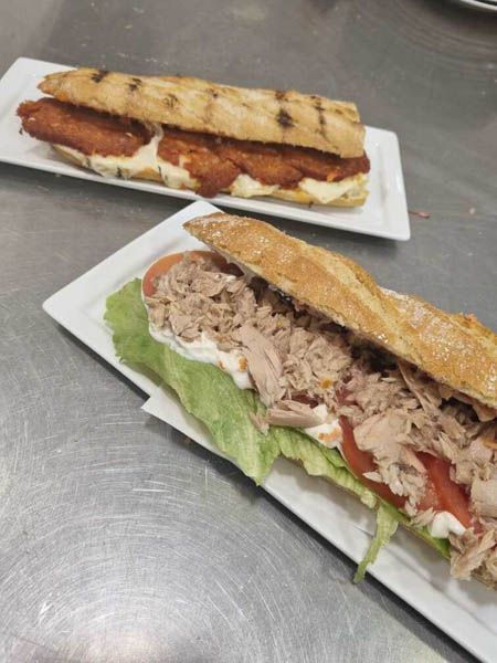 Dos sándwiches están sentados en platos blancos sobre una mesa.