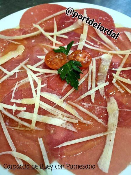 A white plate topped with carpaccio de buey con parmesano