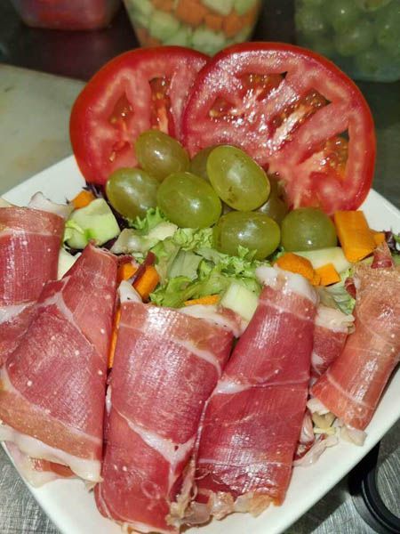 Un plato blanco cubierto con carne y verduras, incluidas uvas y tomates.