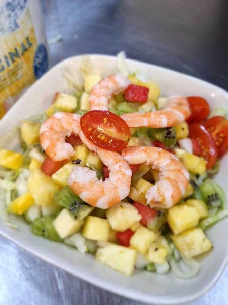 Una ensalada con camarones, piña, kiwi, tomates y lechuga