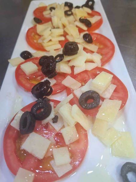Un plato blanco cubierto con tomates, aceitunas y queso.