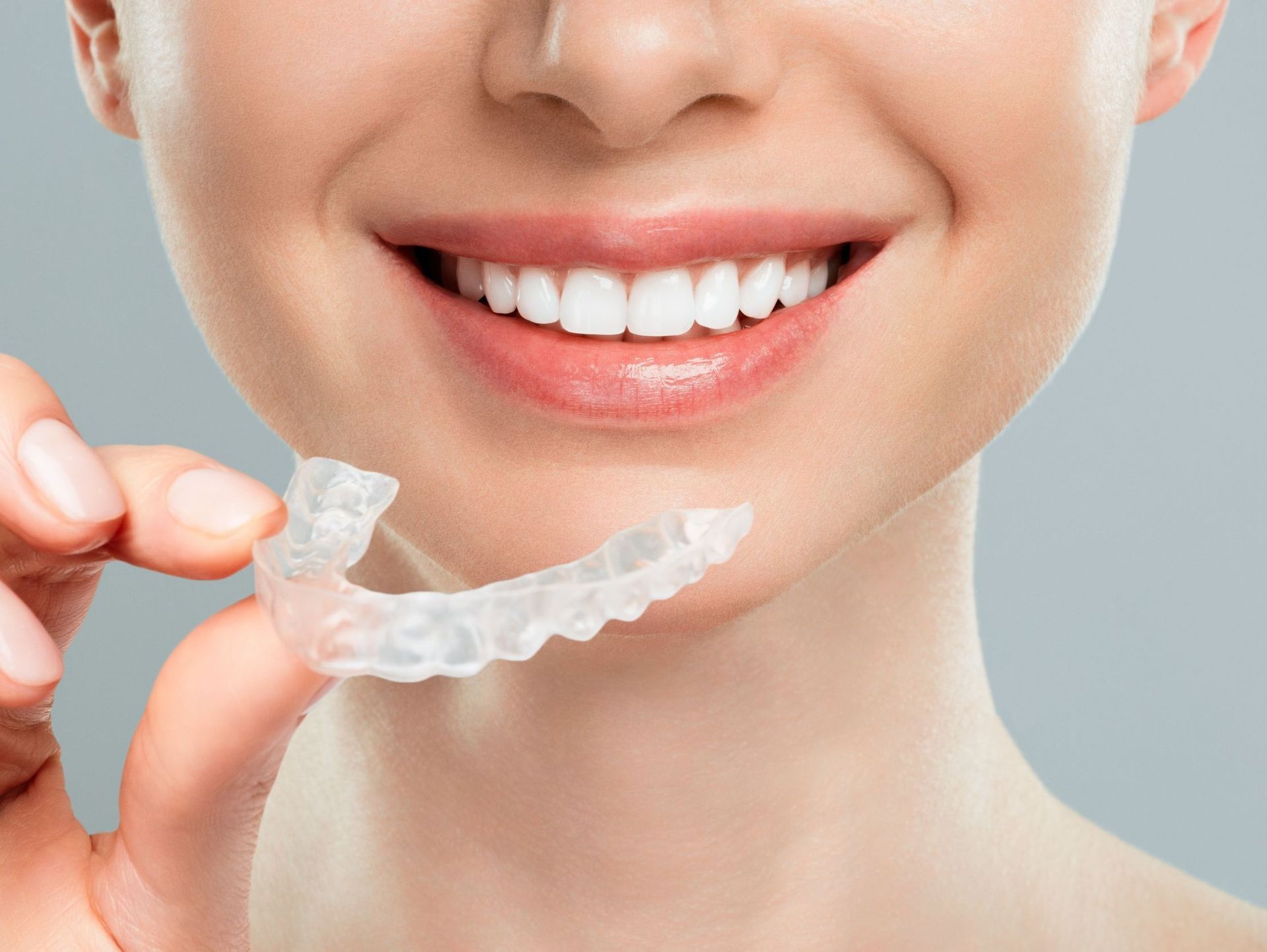 Una mujer sostiene un retenedor transparente delante de sus dientes.