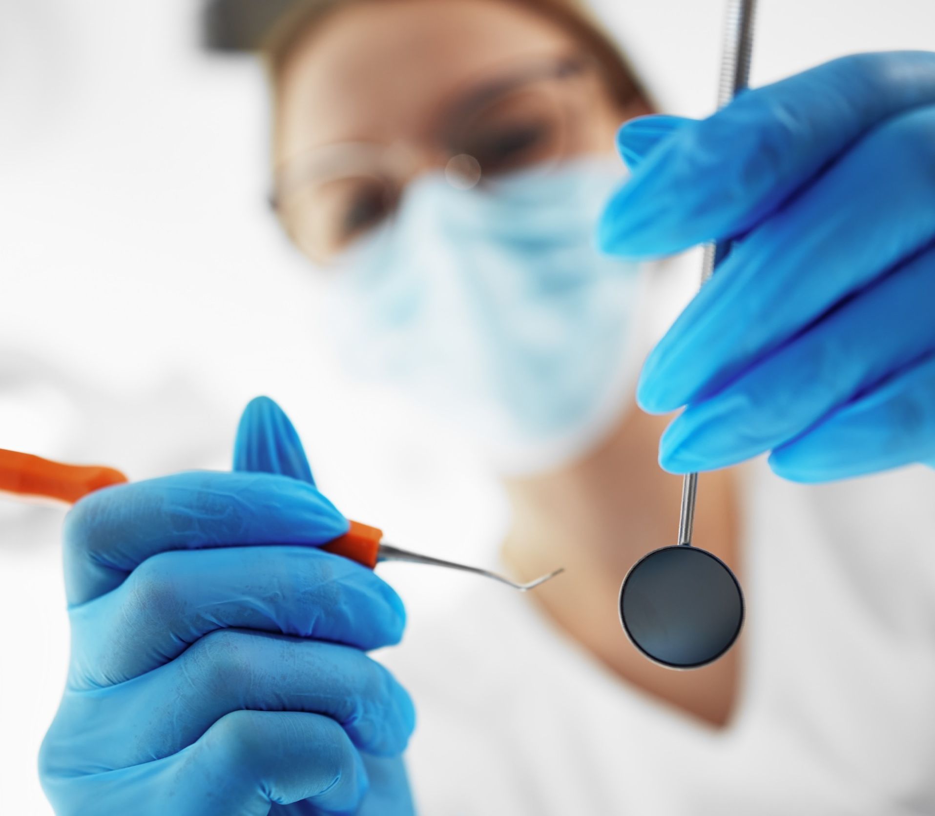 Una mujer con mascarilla y guantes azules sostiene un espejo dental.
