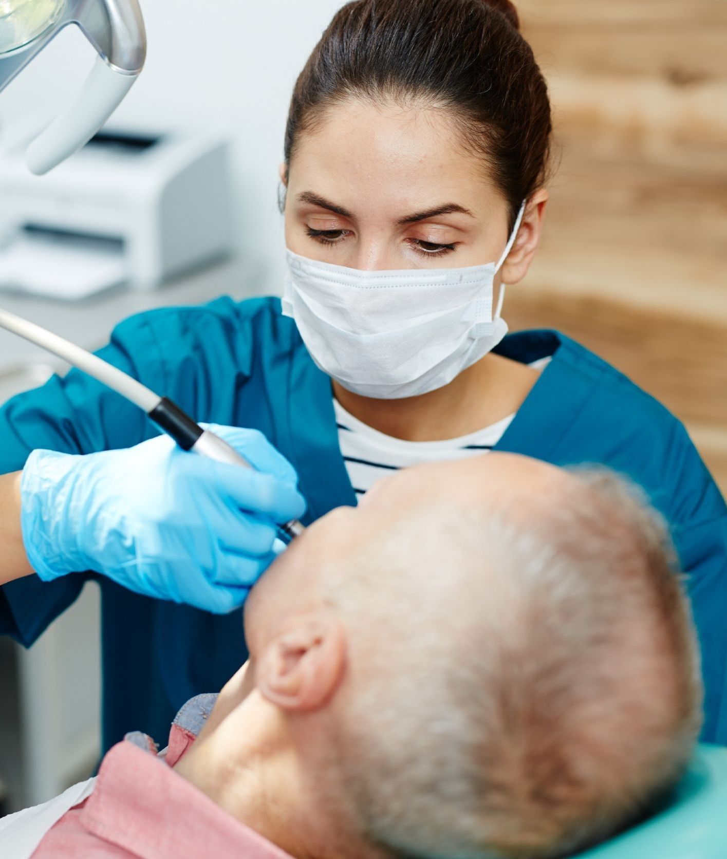 Una dentista con mascarilla examina los dientes de un hombre.