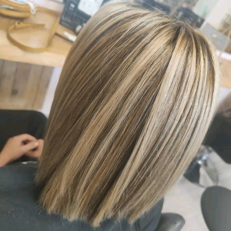 Carré blond avec des mèches foncées et des reflets subtils, dans un fauteuil de salon de coiffure