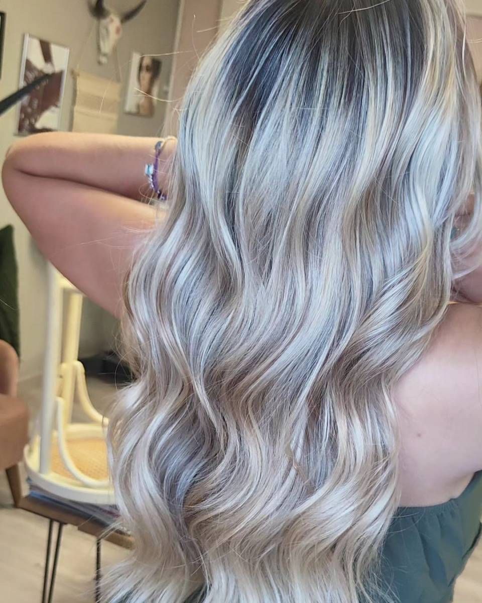 De longs cheveux blond platine ondulés, vus de dos dans une pièce éclairée par un miroir