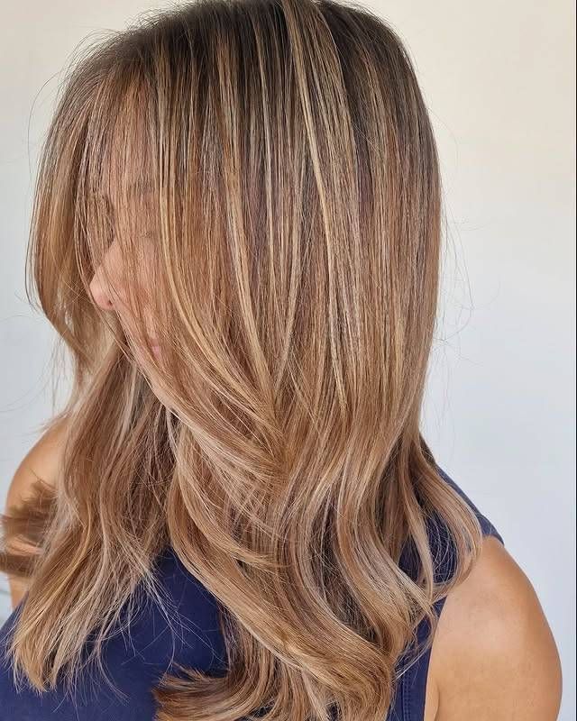 Vue de profil de longs cheveux blonds ondulés aux racines plus foncées, sur un fond clair