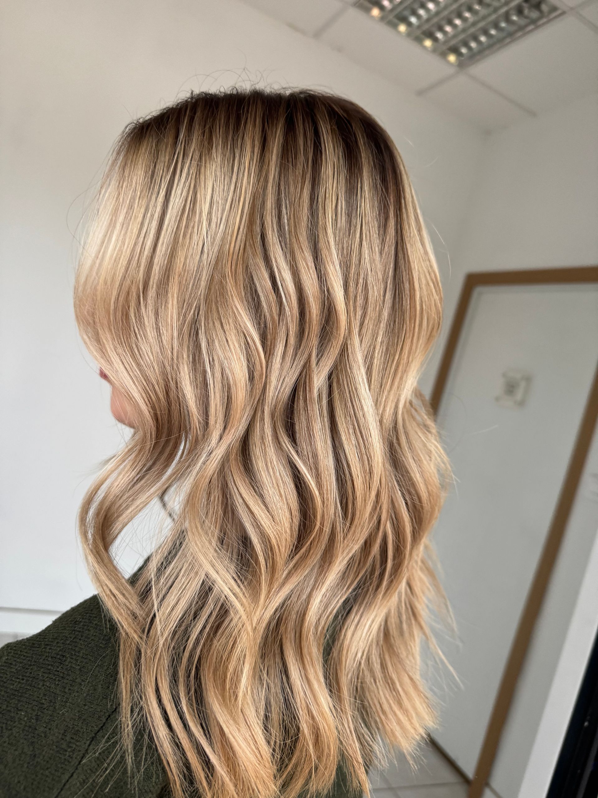 Cheveux blonds méchés et ondulés, mi-longs, dans un salon de coiffure