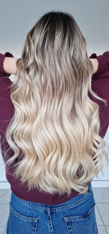 Personne aux longs cheveux blonds ondulés, vue de dos, portant un haut bordeaux et un jean bleu.
