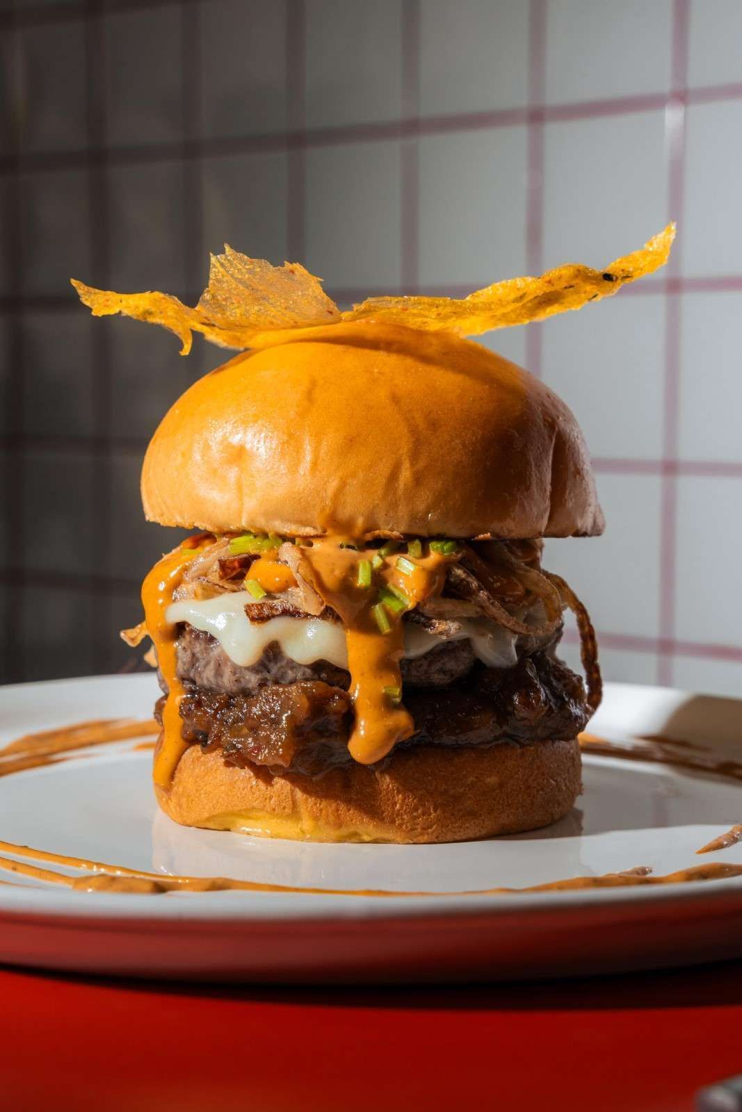 Una hamburguesa gourmet doble con queso, cubierta con salsa y una guarnición crujiente, servida en un plato blanco