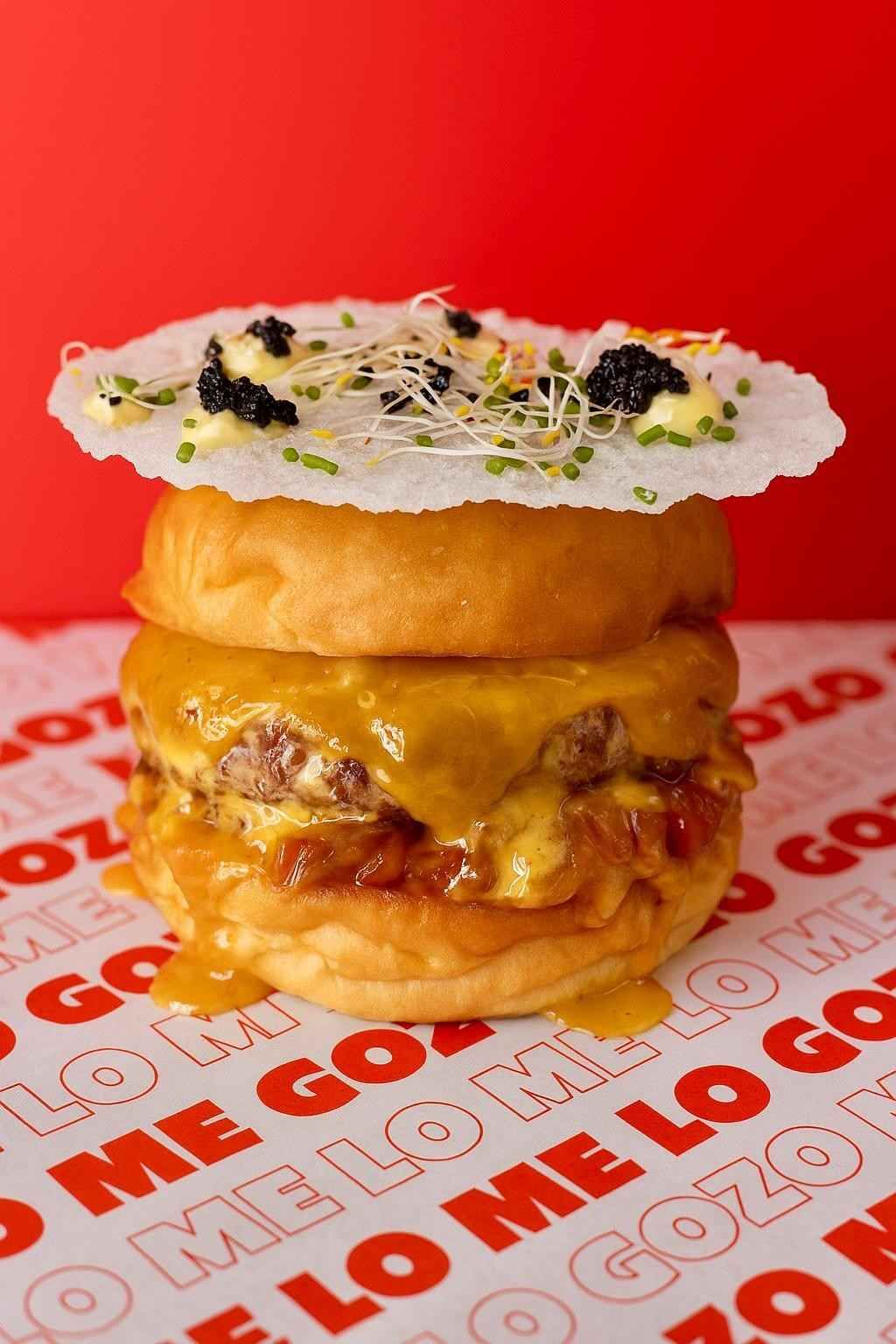 Una hamburguesa con queso cubierta con una galleta de arroz crujiente, caviar, hierbas y brotes