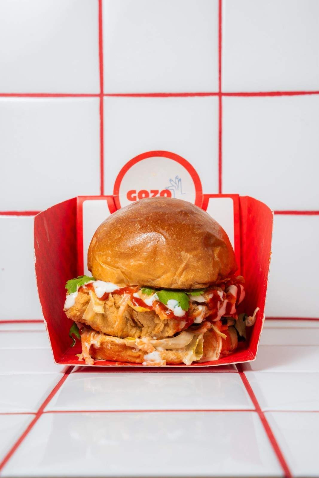 Un sándwich de pollo crujiente en un envase de cartón rojo con el logotipo de la marca