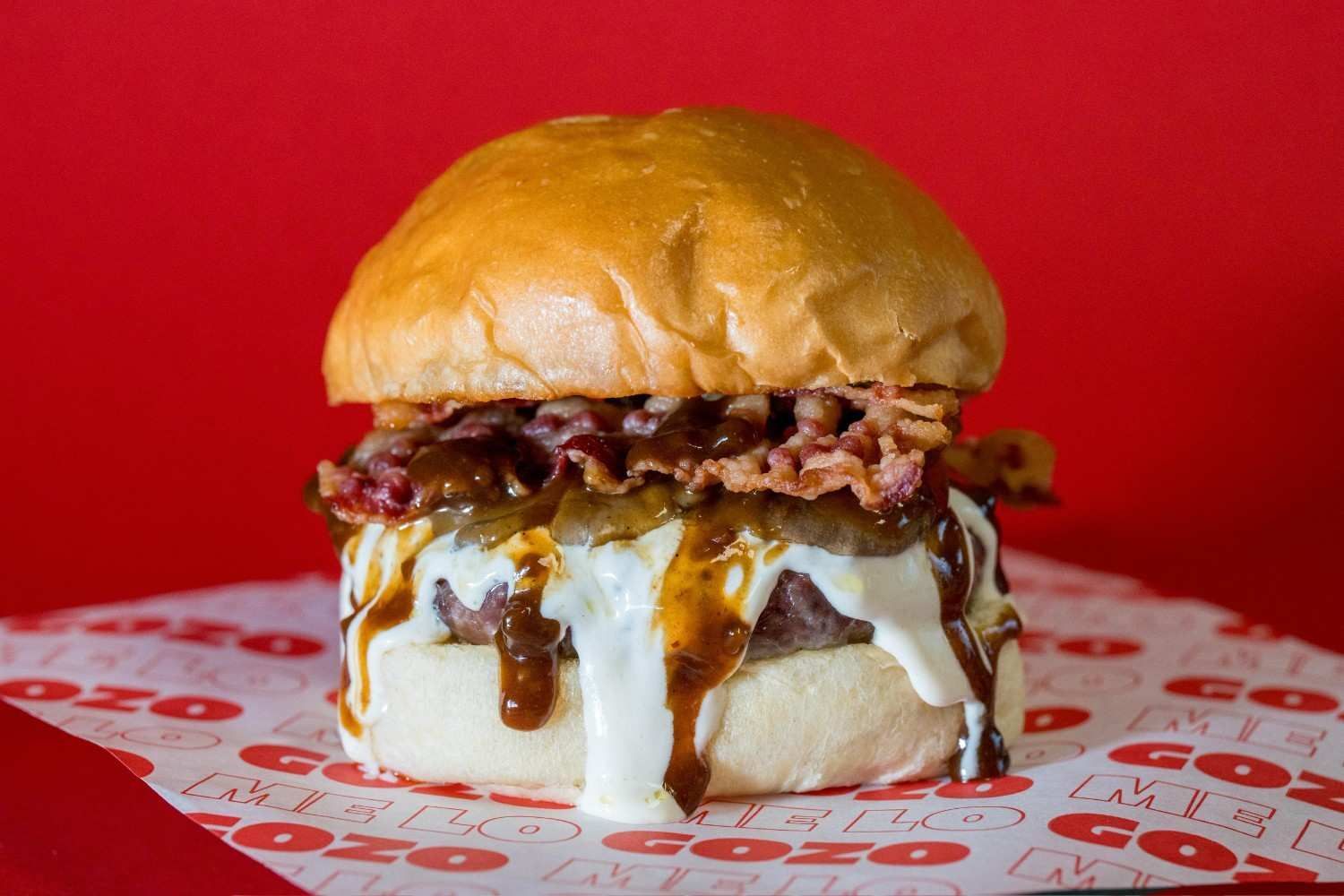 Una jugosa hamburguesa con queso fundido, beicon y salsa, servida sobre un papel con el logotipo de la marca
