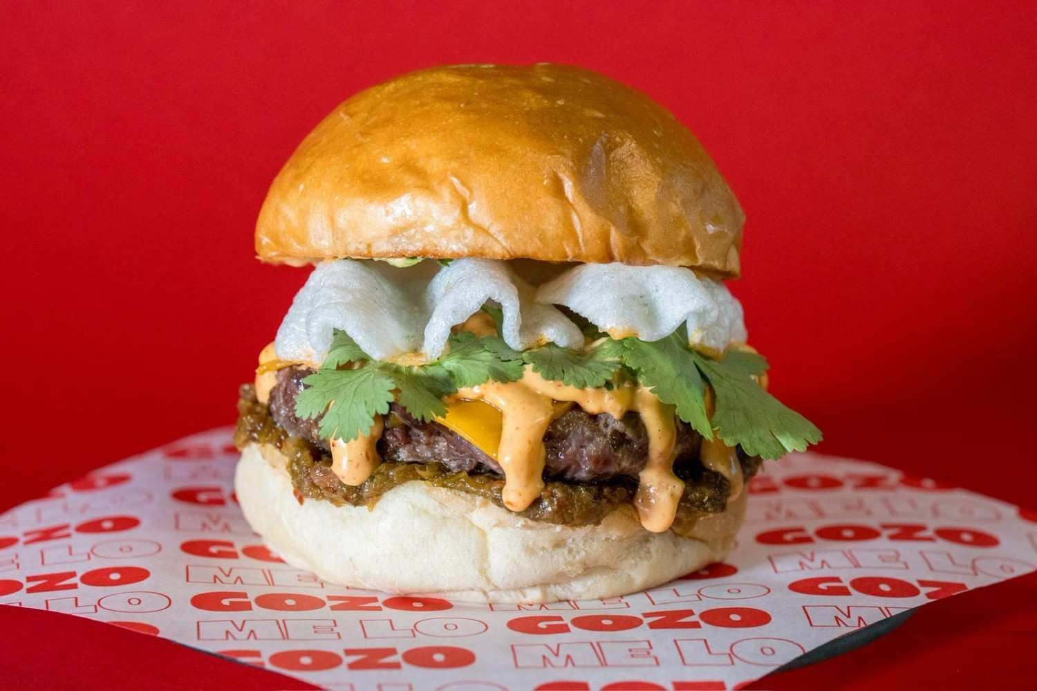 Una hamburguesa gourmet con carne, queso, salsa y verduras, servida en papel pergamino con el logo de la marca