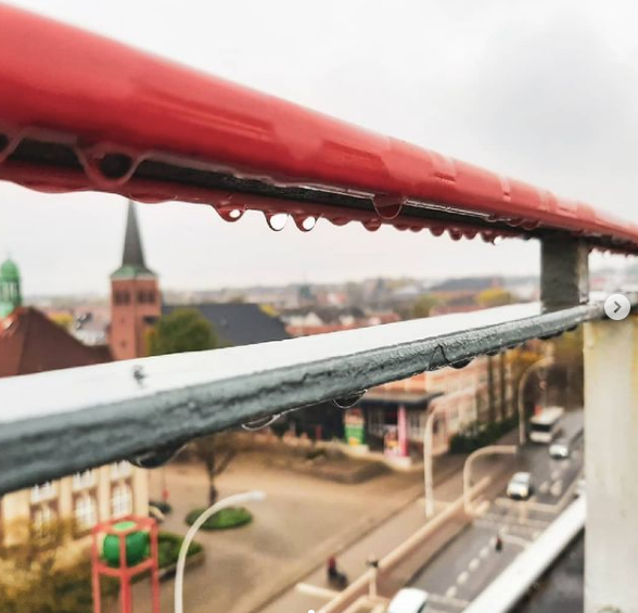 Ein rotes Geländer mit Wassertropfen darauf mit Blick auf eine Stadt