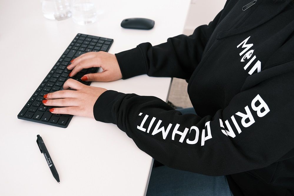 Eine Person tippt auf einer schwarzen Tastatur und trägt ein schwarzes Sweatshirt mit der Aufschrift