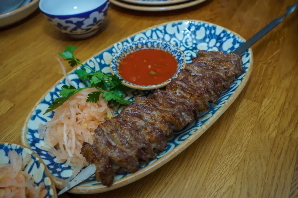 Un pincho de kebab a la parrilla servido en un plato con estampado azul y blanco, acompañado de salsa roja para mojar.