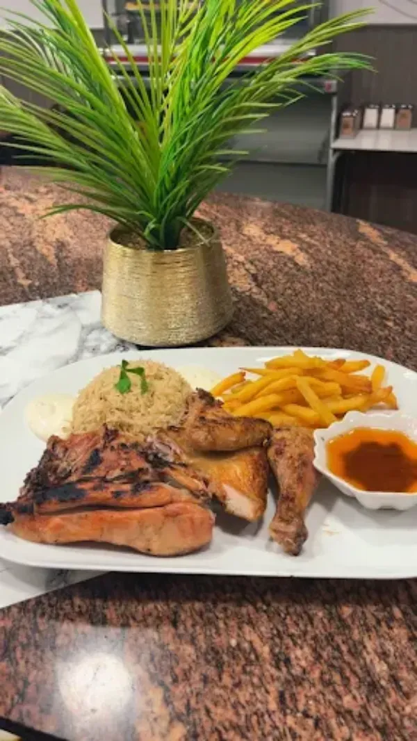 Un plato blanco con pollo a la parrilla, arroz amarillo, papas fritas y un pequeño recipiente con salsa para mojar.
