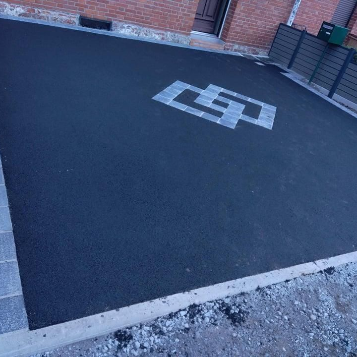 Allée en asphalte noir avec un motif géométrique gris, bâtiment en briques et bordure grise.