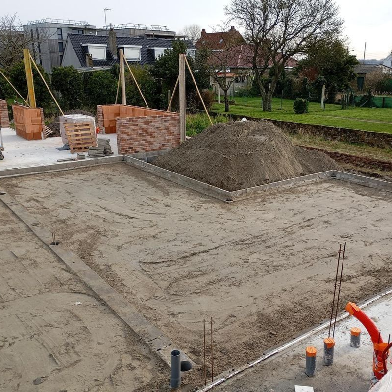 Chantier de construction avec terrain nivelé, tas de briques et un tas de terre, prêt pour la construction.