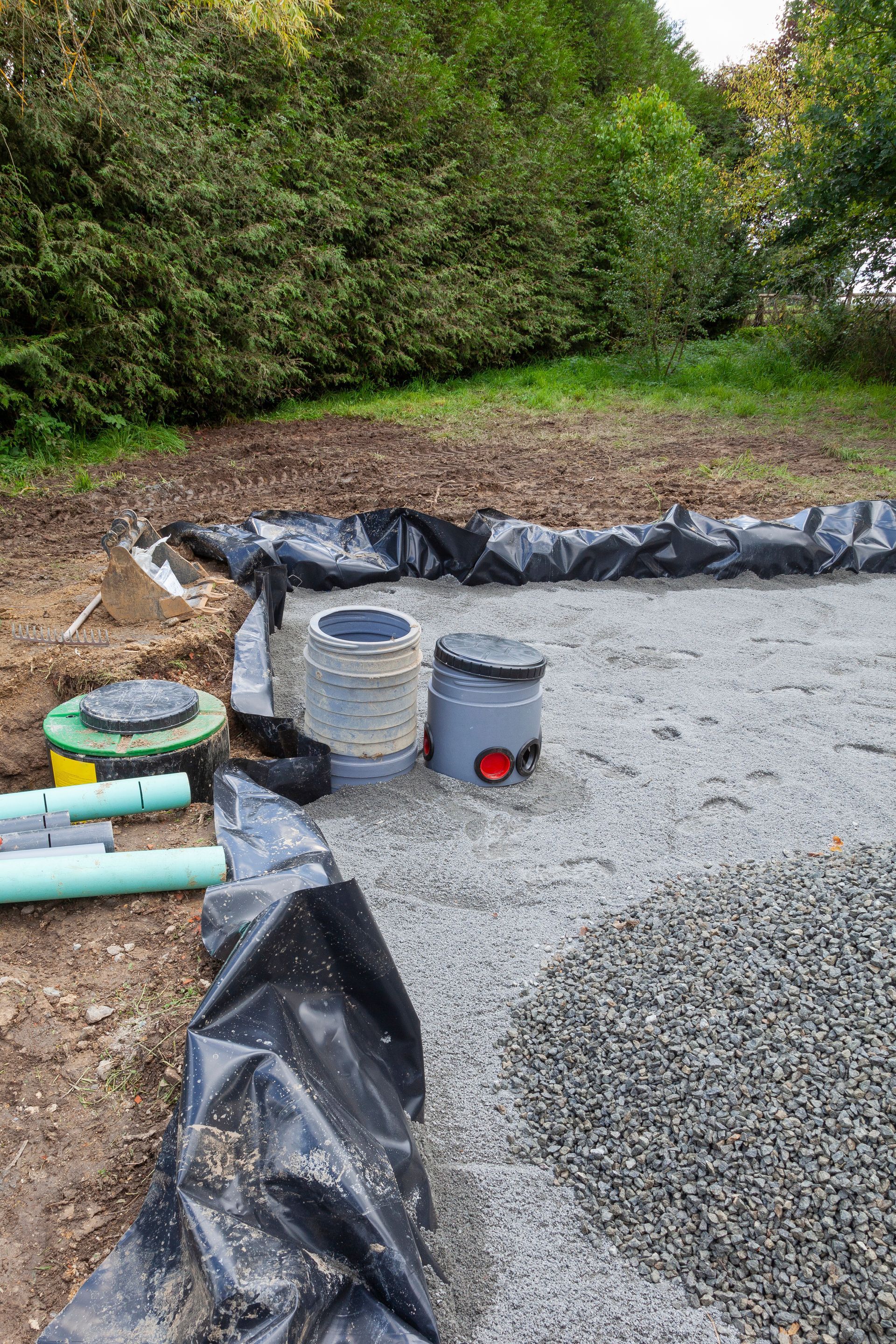 Chantier de construction avec gravier, tuyaux et réservoirs délimités par du plastique noir.
