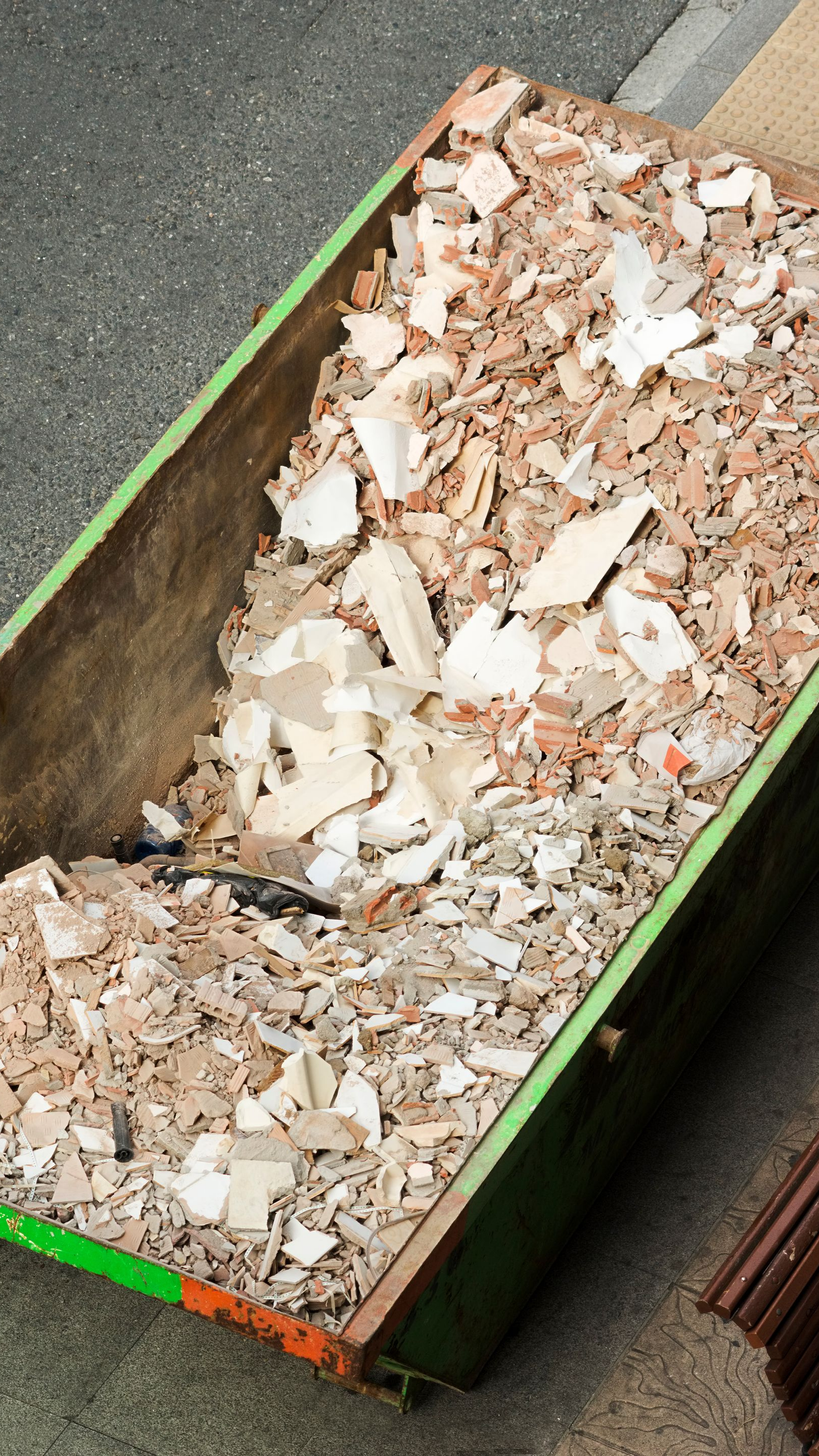 Benne verte remplie de débris de construction, notamment des carreaux cassés et du plâtre.