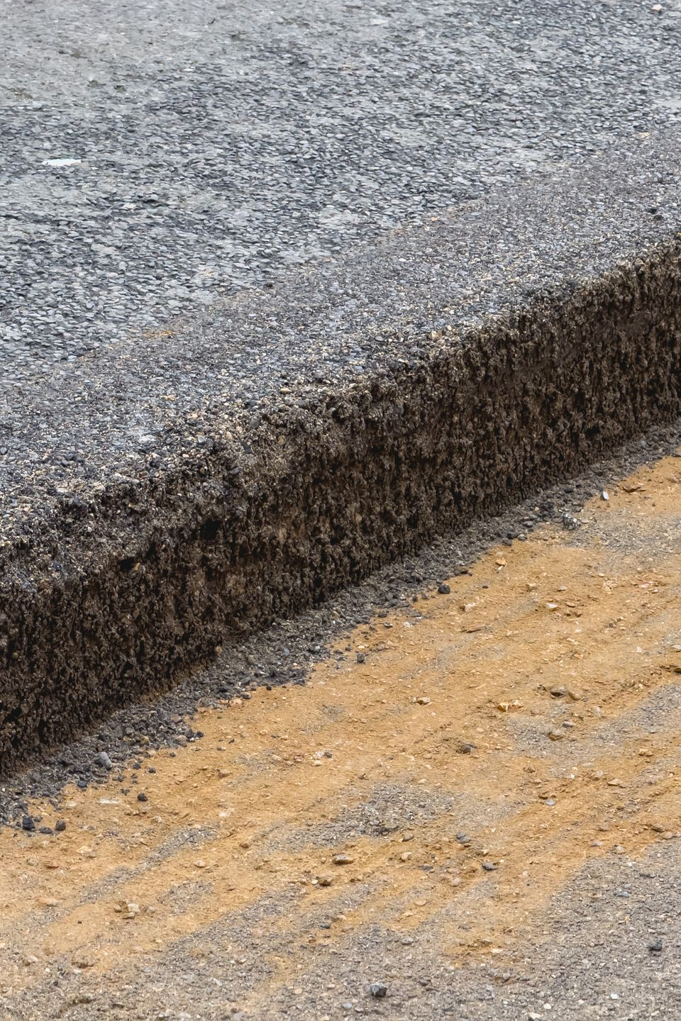 Coupe transversale d'une route asphaltée montrant les différentes couches : surface en gravier, base en agrégats foncés et sous-couche de sable.