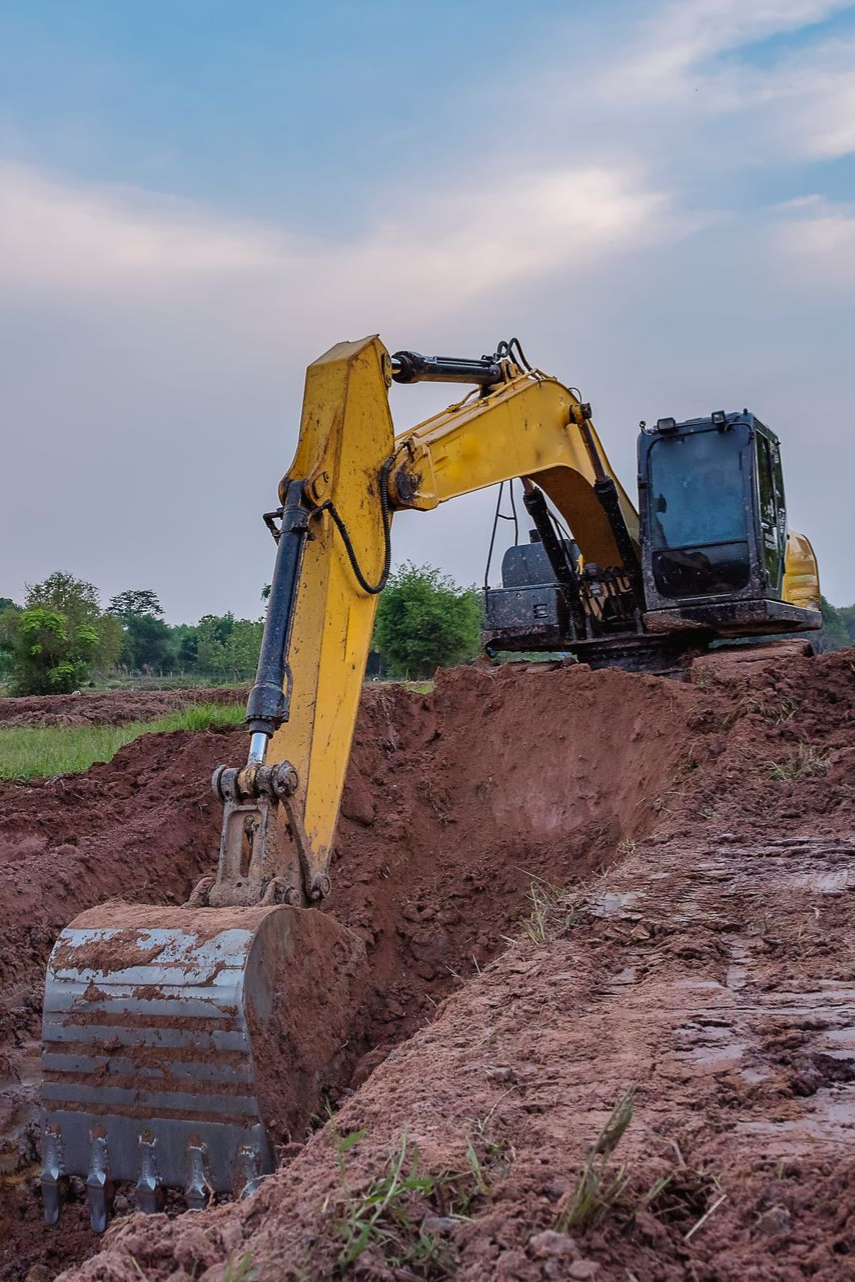 Une pelleteuse jaune creuse une tranchée dans un sol brun sous un ciel bleu.