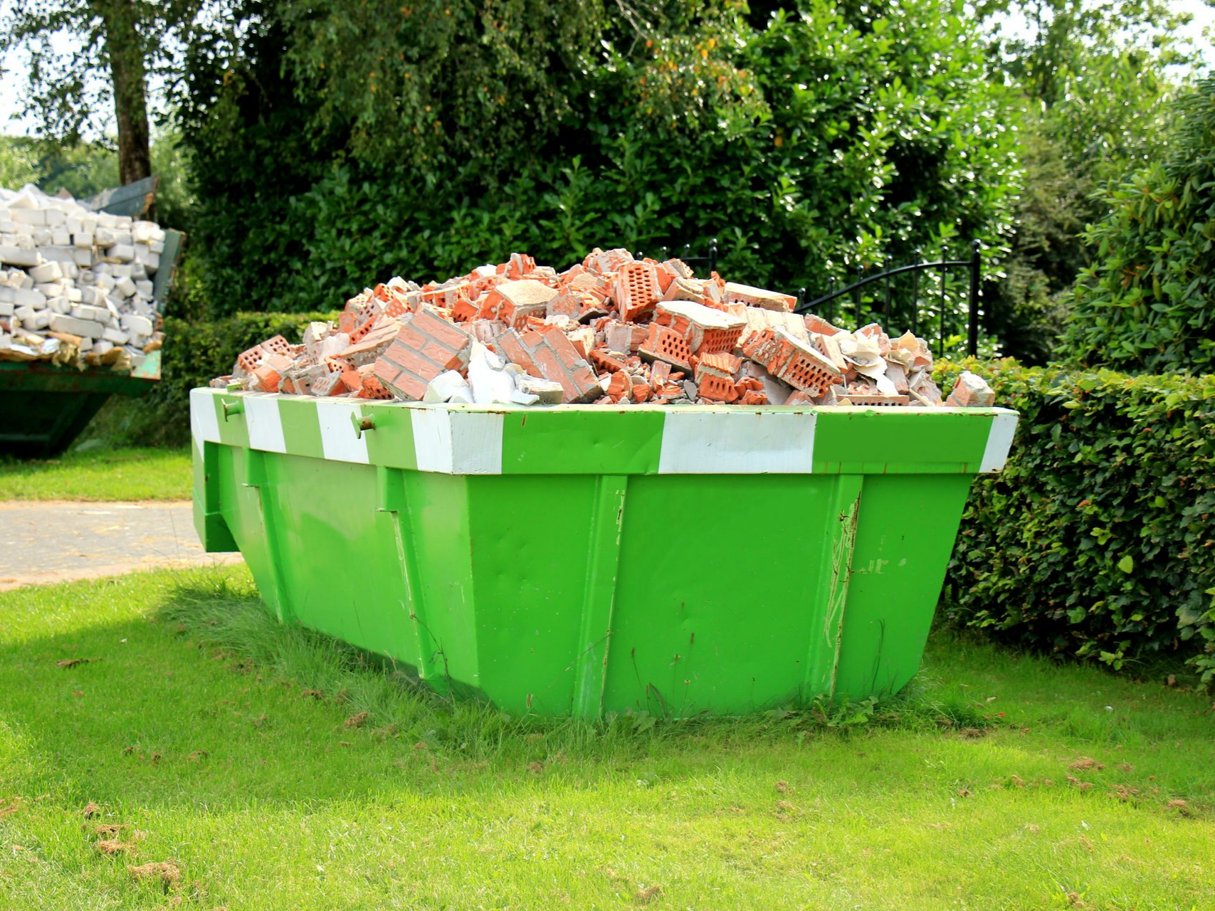 Une benne à ordures verte remplie de briques rouges sur une pelouse.