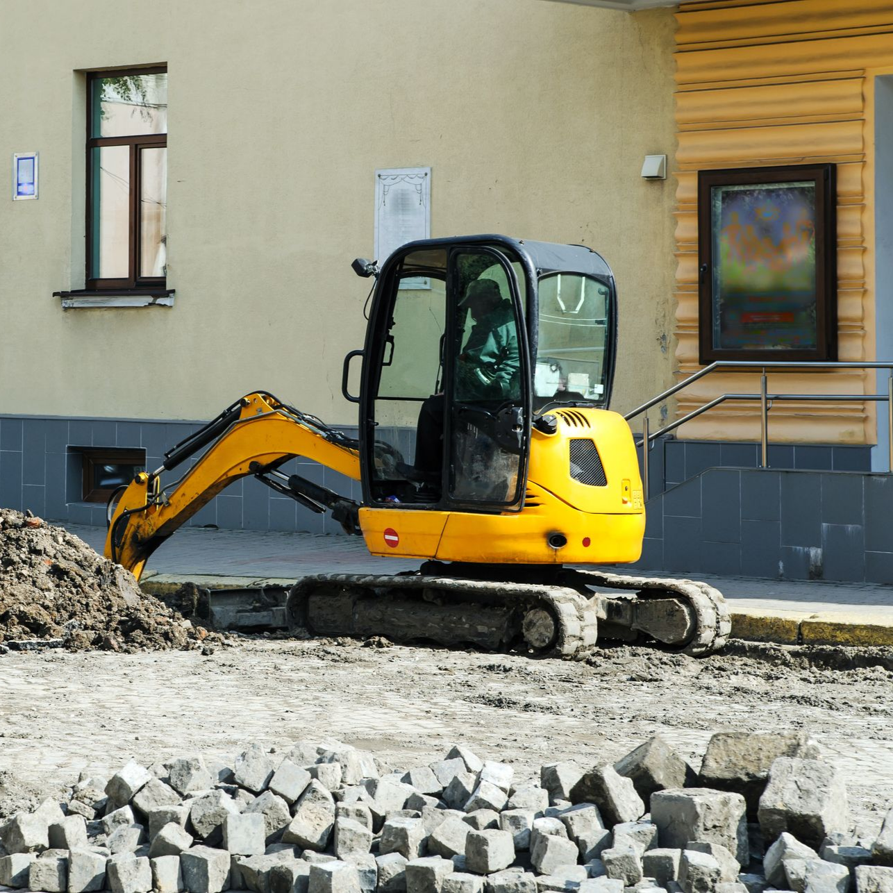 Une mini-pelle jaune est en action sur un chantier de construction, en train d'enlever des débris près d'un bâtiment.