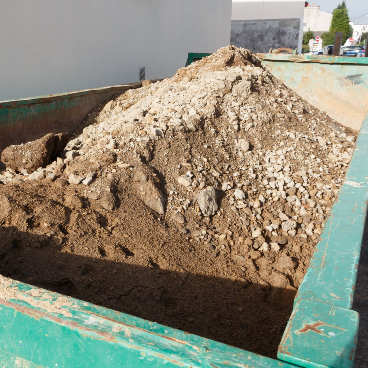 Tas de terre et de gravier dans une benne verte, à l'extérieur au soleil.
