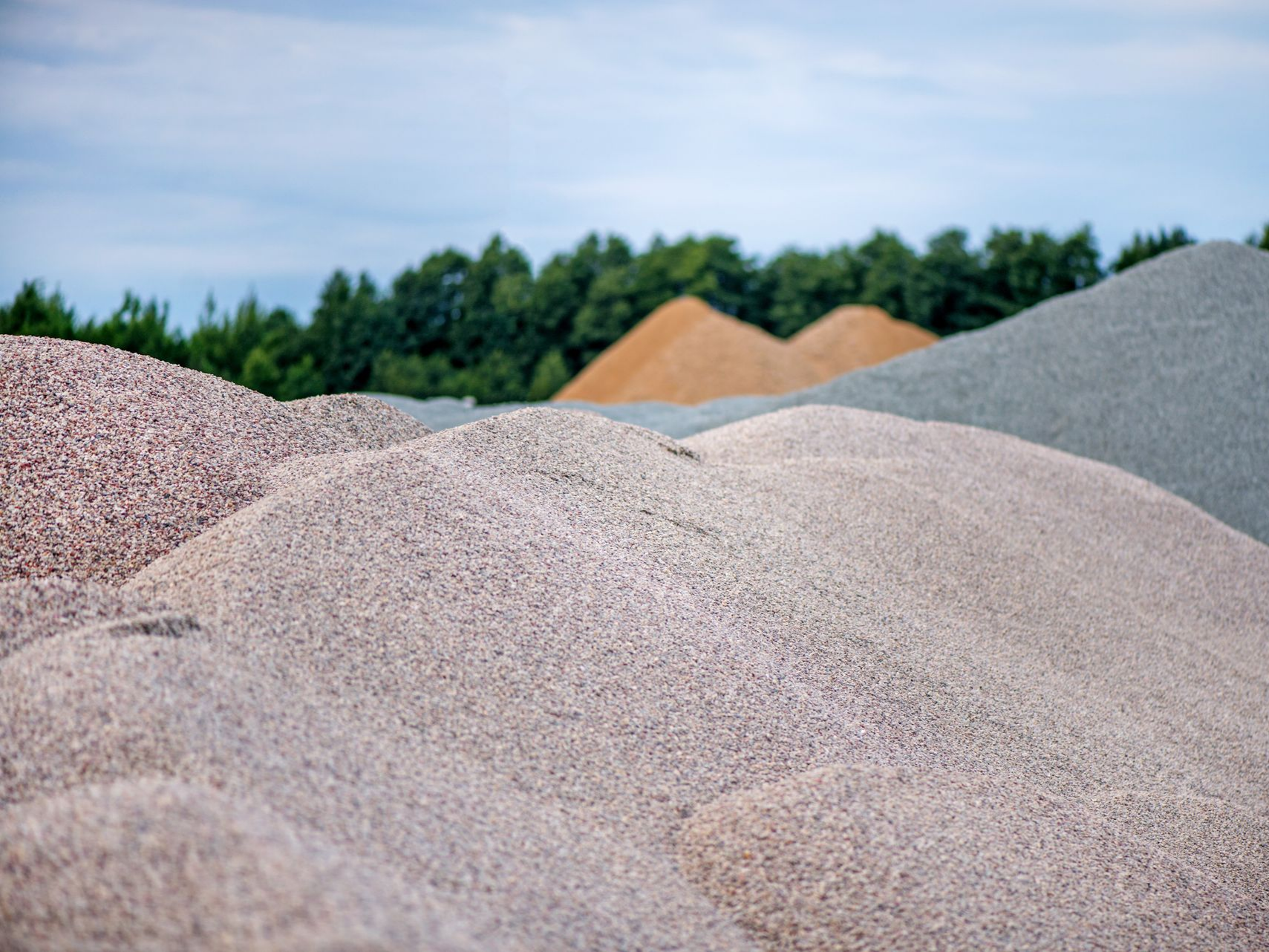 Des tas de gravier de couleurs variées avec des arbres et un ciel nuageux en arrière-plan.