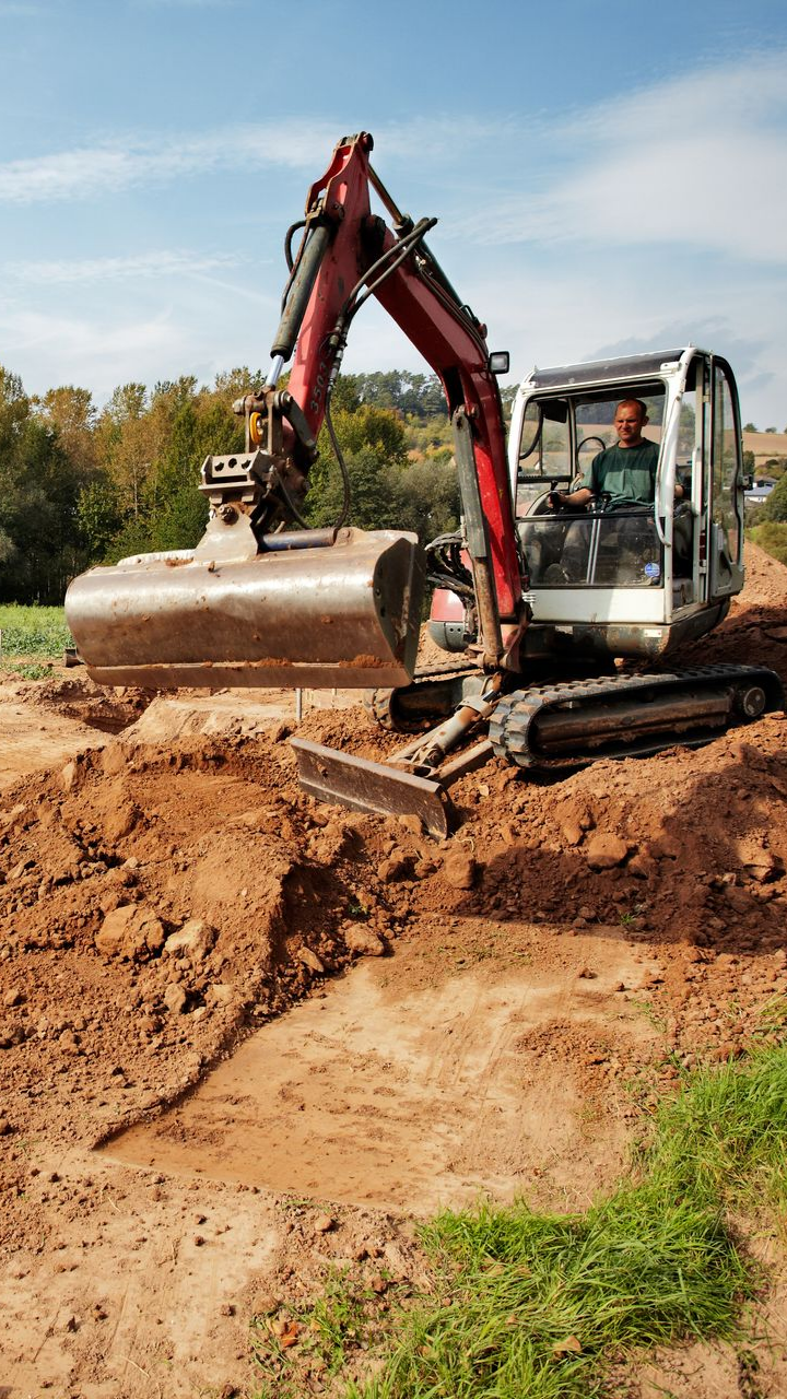 Une excavatrice creuse la terre par une journée ensoleillée ; l'opérateur est dans la cabine.