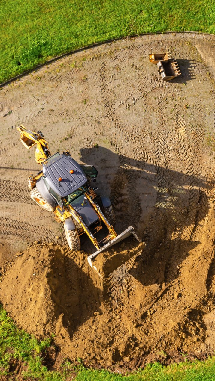 Des excavatrices creusent sur un chantier de construction, entourées de terre et d'herbe.