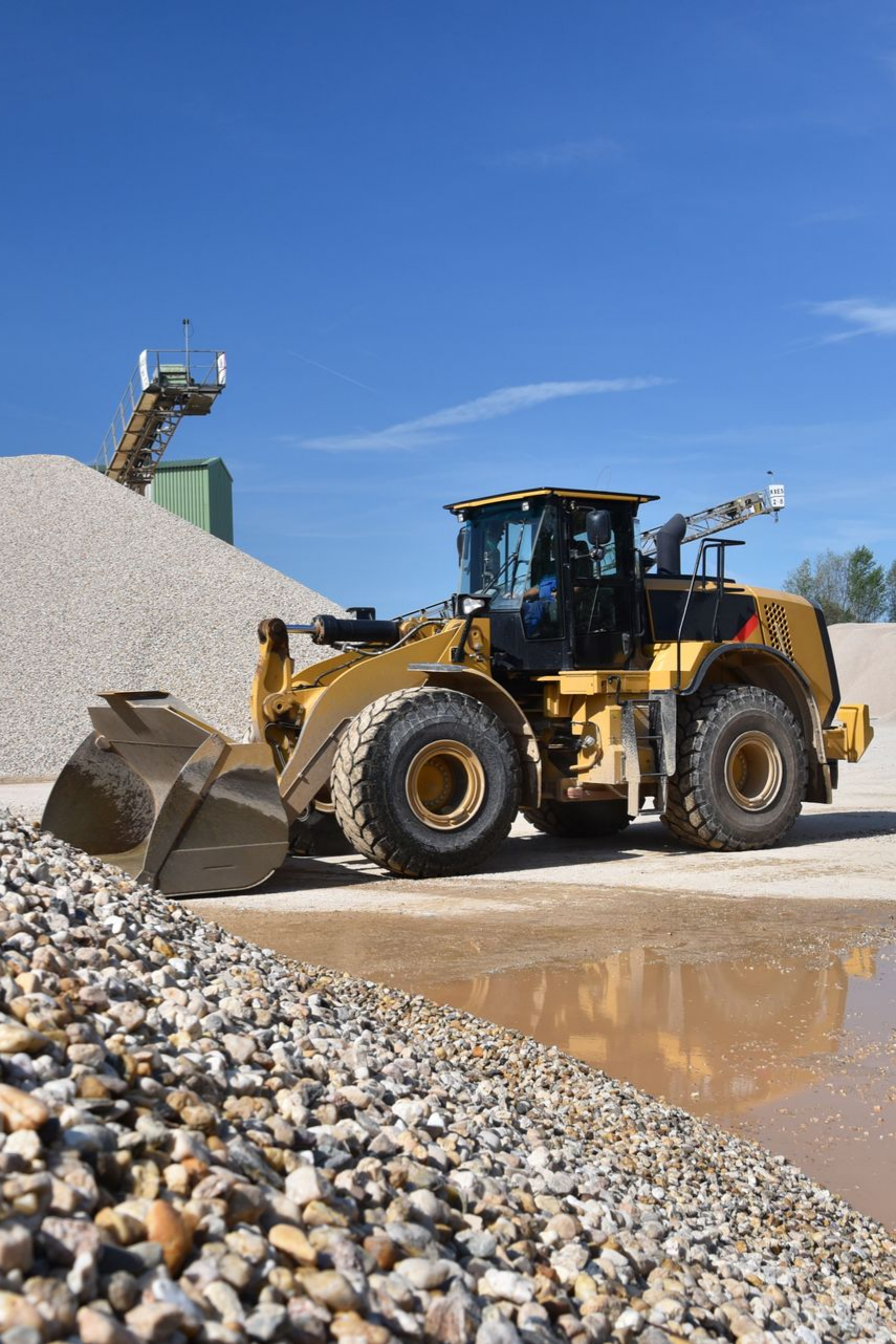 Chargeuse Caterpillar jaune sur un tas de gravier. Ciel bleu, tapis roulant et eau en arrière-plan.