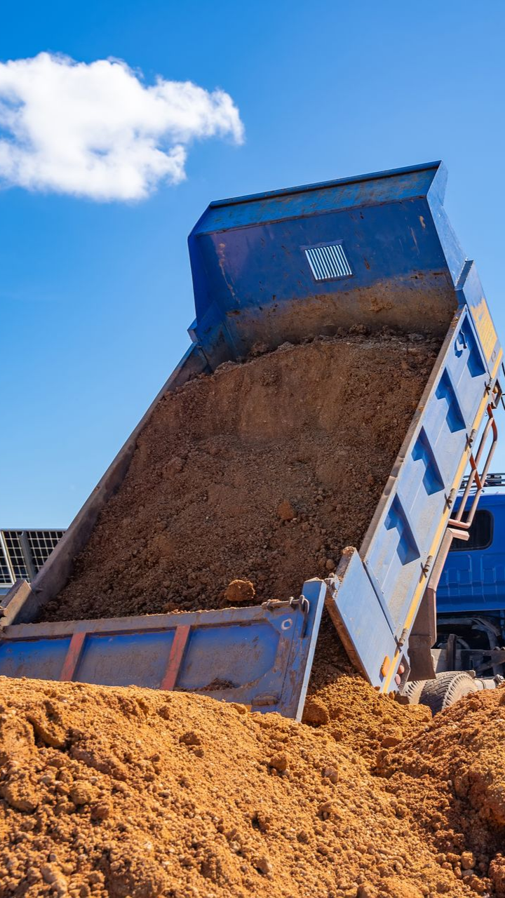 Un camion-benne bleu décharge de la terre brune sur fond de ciel bleu.