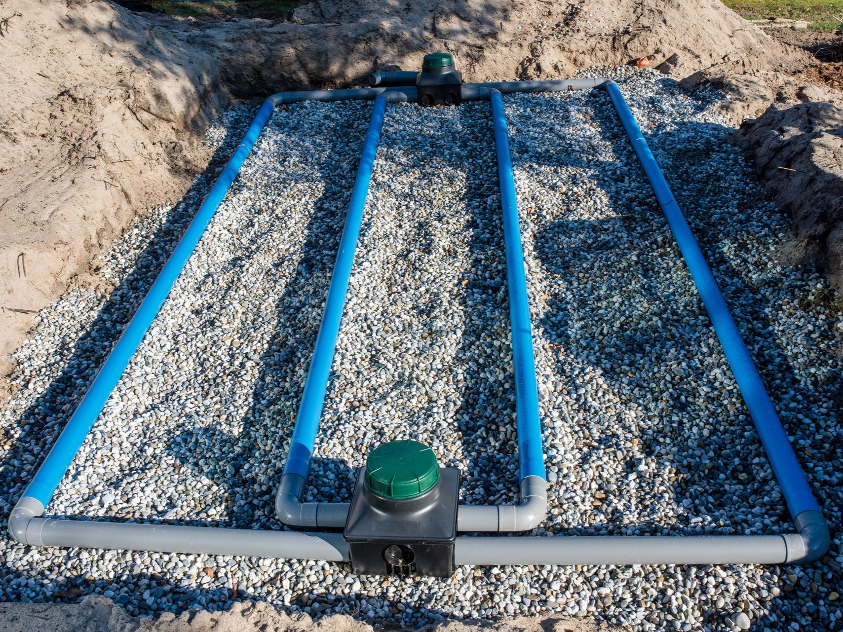 Tuyaux bleus posés dans du gravier, faisant partie d'un champ d'épandage d'une fosse septique, dans une tranchée sablonneuse.