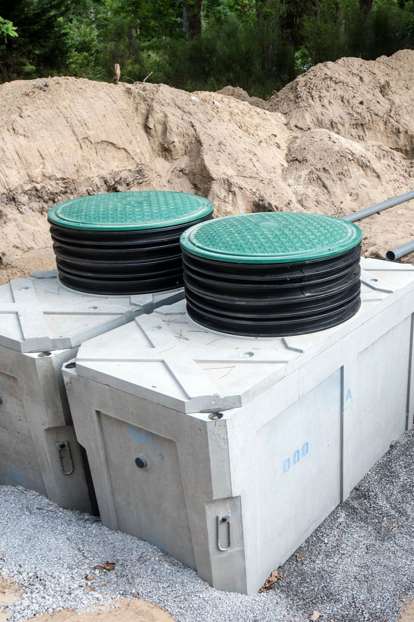 Deux fosses septiques en béton avec couvercles verts, à l'extérieur.