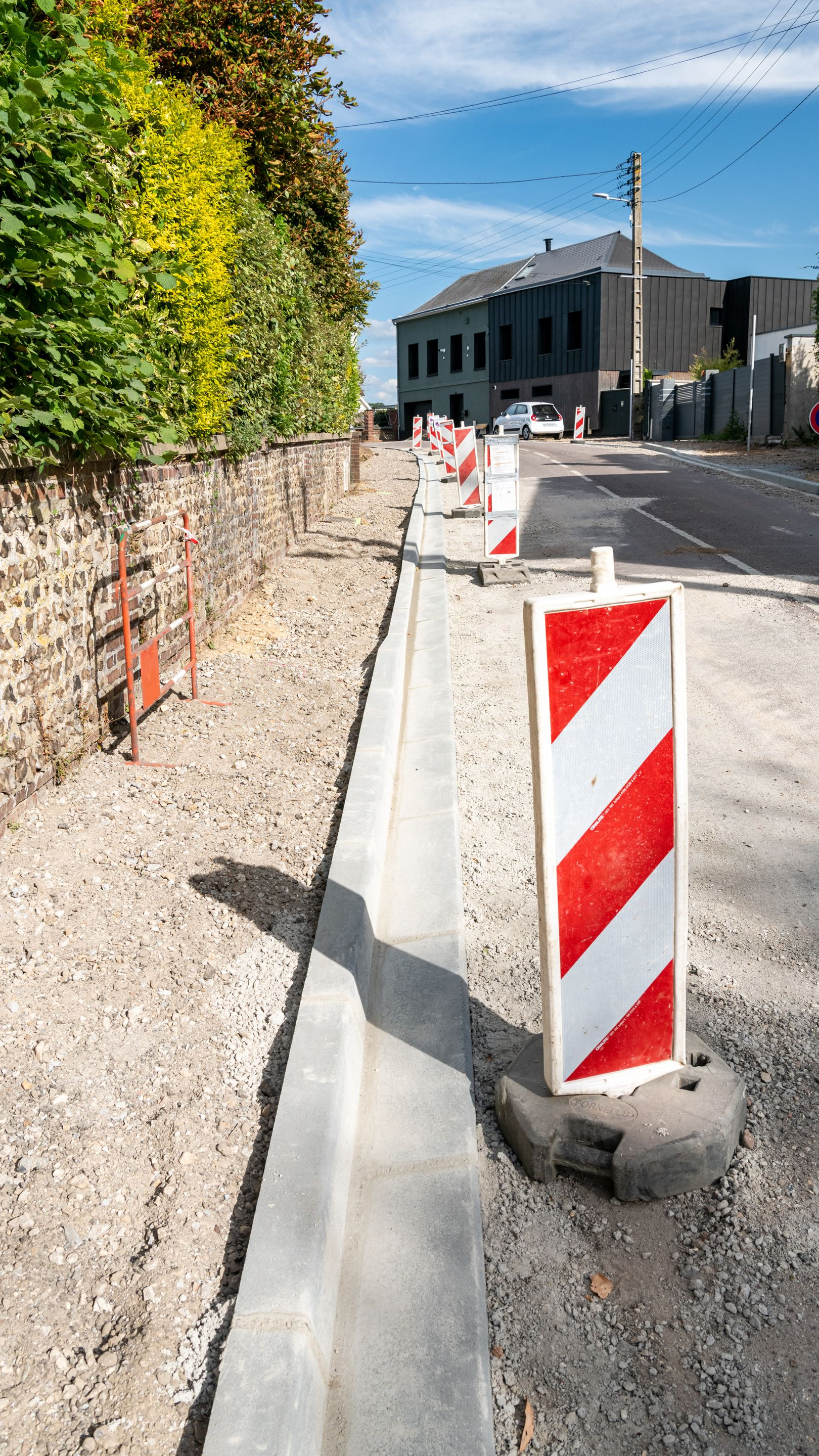 Travaux routiers avec bordure en béton, barrières orange et blanches.