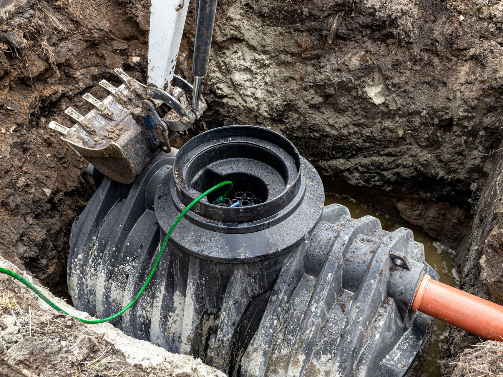 Une fosse septique noire est installée dans un trou creusé dans le sol à l'aide d'une excavatrice.